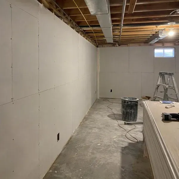 New drywall sheets hung on basement walls with a gap above the concrete slab