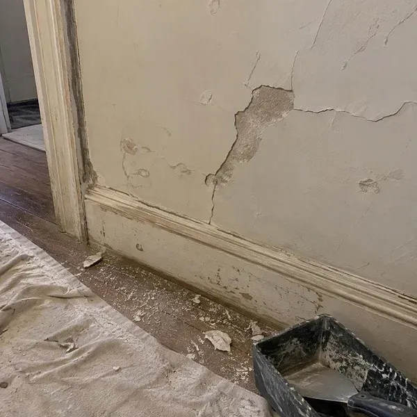 Cracked plaster wall above an old baseboard in an older home