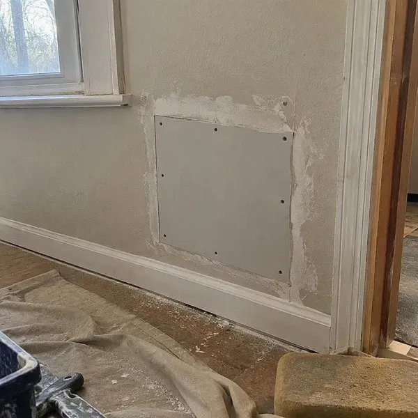 Square drywall patch secured above a baseboard during a rental repair