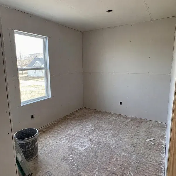 New construction drywall hung in an empty room with unfinished floor