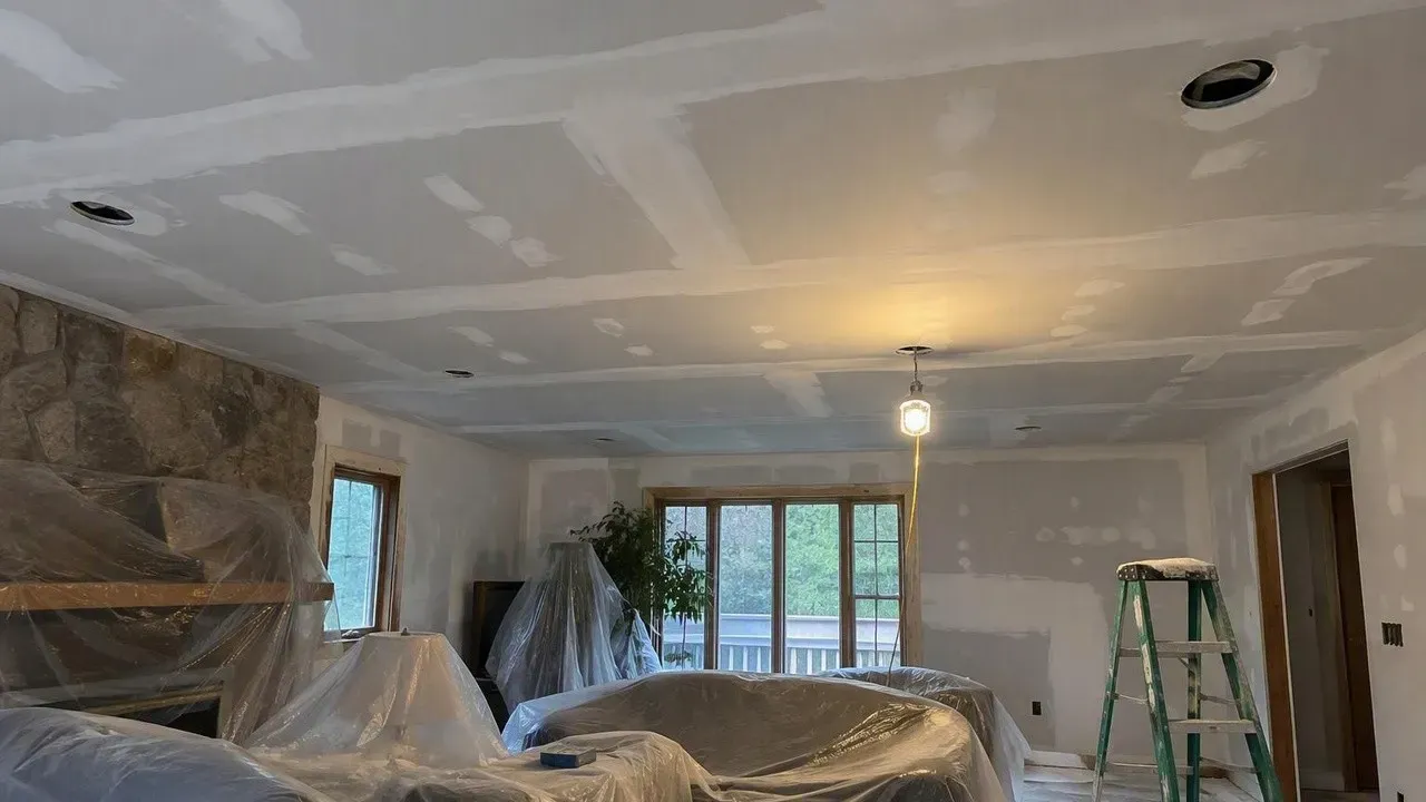 New smooth drywall ceiling above furniture protected with plastic after popcorn ceiling removal